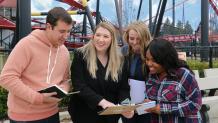 Group of students with female marketing professional in a suit looking at a clipboard in front of X Flight