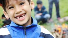 Boy smiling outside by the fire at the Scout Day Event.